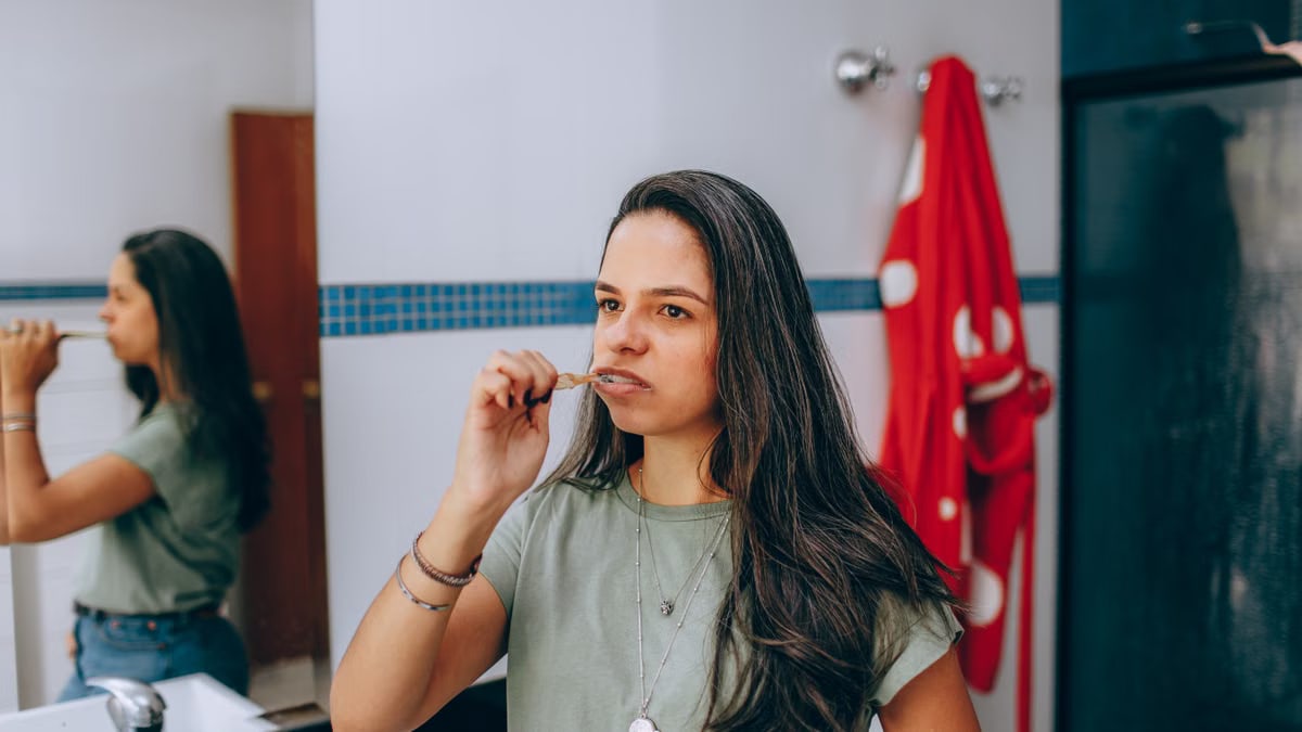 Young woman brushing teeth in a modern bathroom with a red towel hanging nearby.