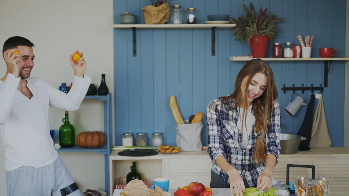 Attractive loving couple having fun in the kitchen. Handsome man juggle with fruits to impress his girlfriend at home